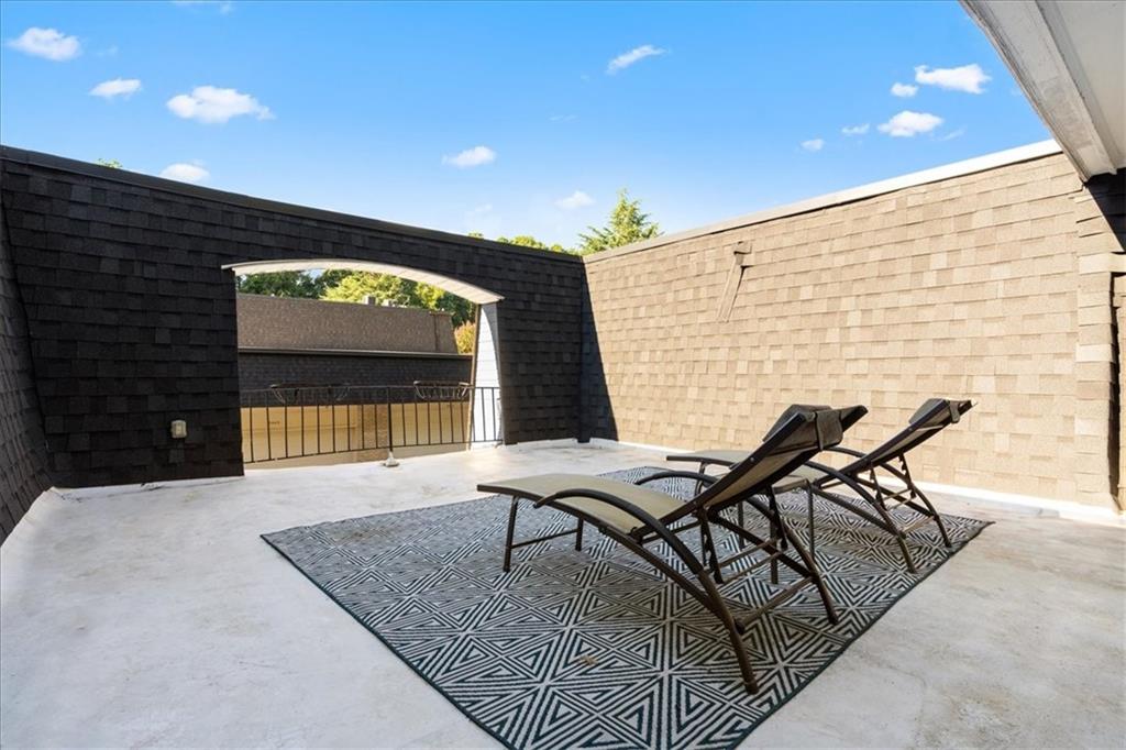 Rooftop patio with two reclining lounge chairs on a geometric rug between dark and light shingle walls.