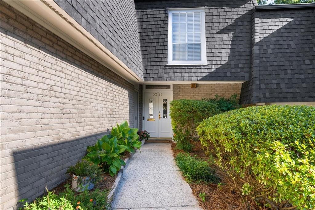 Home entrance with a recessed white door, brick walls, dark shingles, and landscaped walkway.
