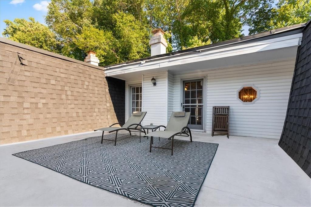 Rooftop patio with two lounge chairs on a geometric rug beside white siding.