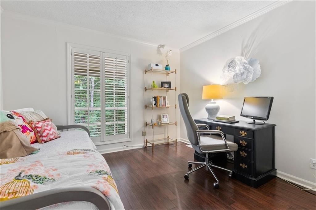 Bedroom and home office with a shuttered window, dark desk, and hardwood floors.