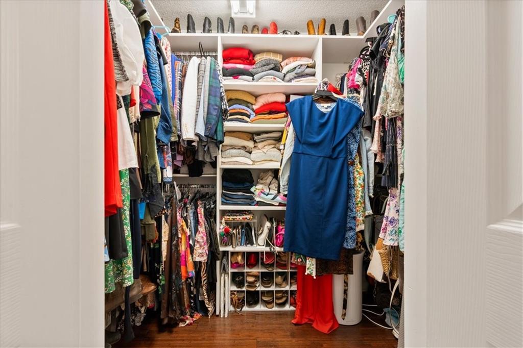 Walk-in closet with colorful clothing, folded garments, shoe cubbies, and dark wood flooring.