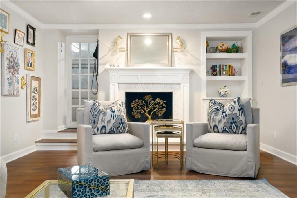 Staged living room with a white fireplace, built-in shelves, and two gray armchairs with blue patterned cushions.