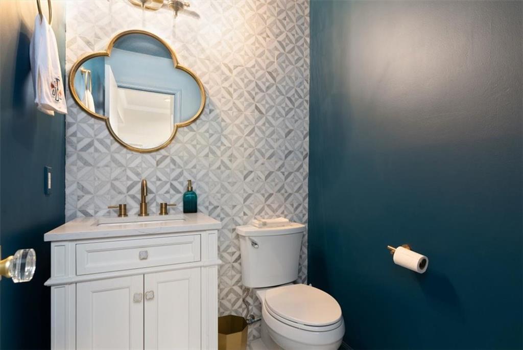 Powder room with geometric tile, a white vanity, and a gold-framed clover-shaped mirror.