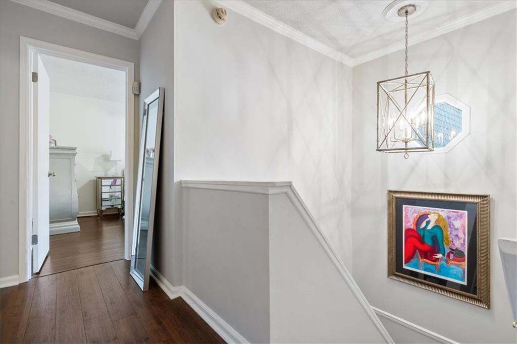 Hallway and stair landing with dark wood floors, a geometric pendant light, and colorful framed artwork.