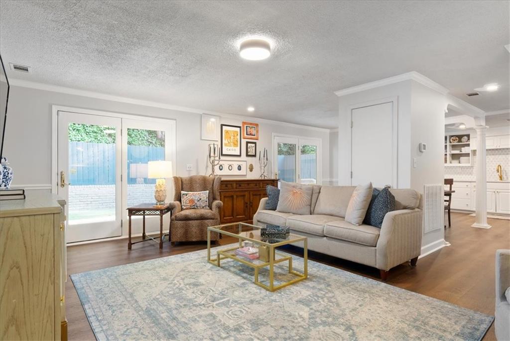 Living room with a beige sofa, patterned rug, French doors, and an adjoining white kitchen.