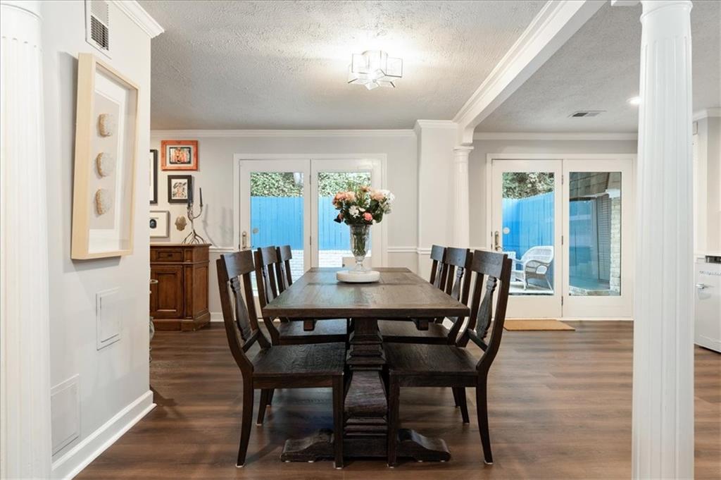 Dining room with a dark wood table, white columns, and glass doors overlooking a blue pool.