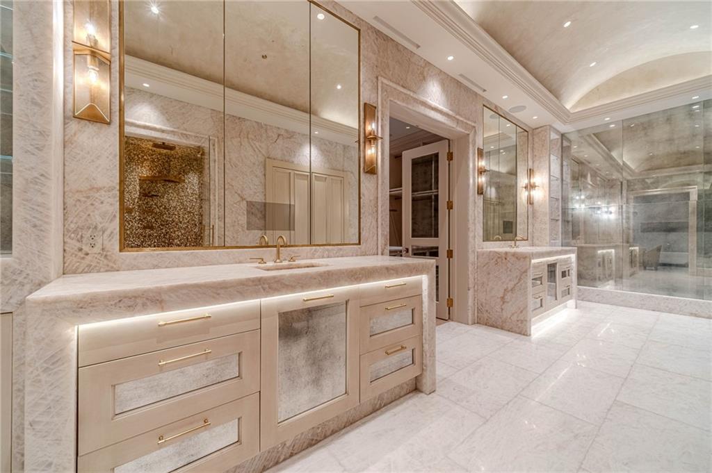 Marble bathroom with twin vanities, gold fixtures, and a glass-enclosed shower.
