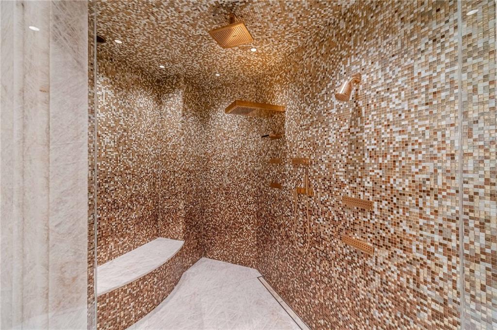 Mosaic-tiled walk-in shower with a ceiling rain showerhead and pale stone benches.