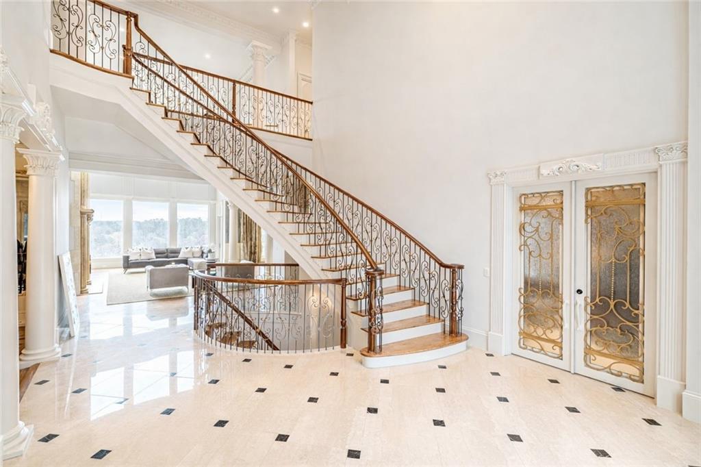 Spacious foyer with a sweeping iron-railed staircase, patterned glass doors, and pale stone flooring.
