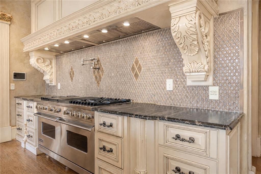 Kitchen with ornate cream cabinetry, a stainless double-oven range, and diamond-pattern tile backsplash.