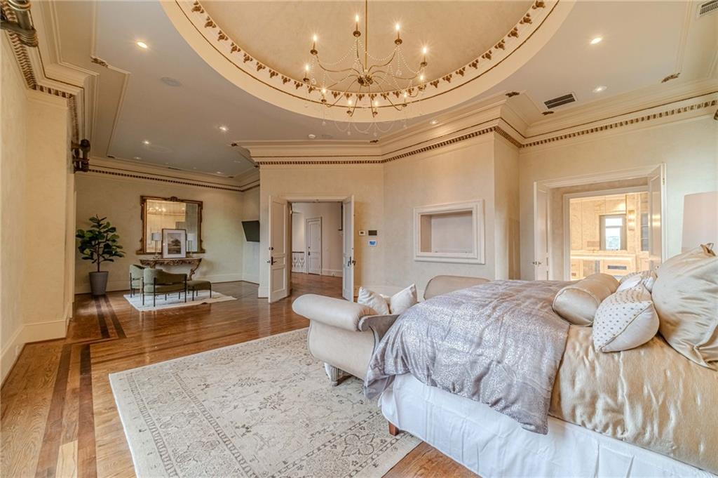 Spacious bedroom with an ornate tray ceiling, chandelier, hardwood floors, and a separate sitting area.