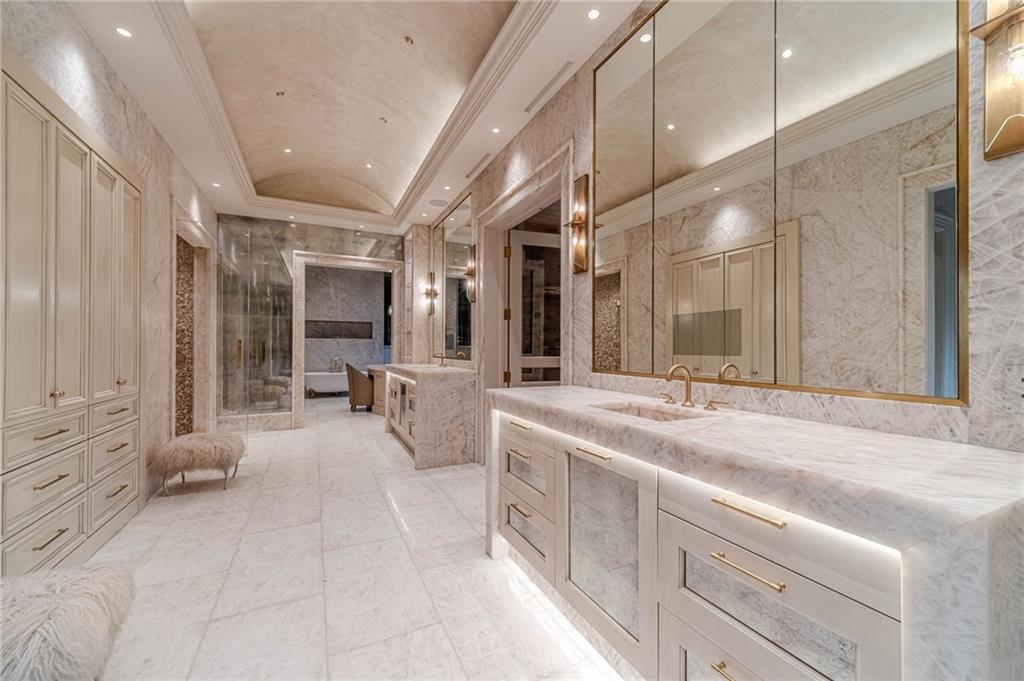 Marble bathroom with a long double vanity, gold fixtures, mirrored cabinets, and a glass-enclosed shower.
