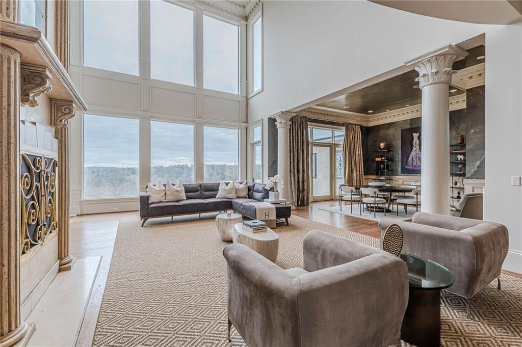 Double-height living room with tall tree-facing windows, an ornate stone fireplace, and an adjoining dining area.