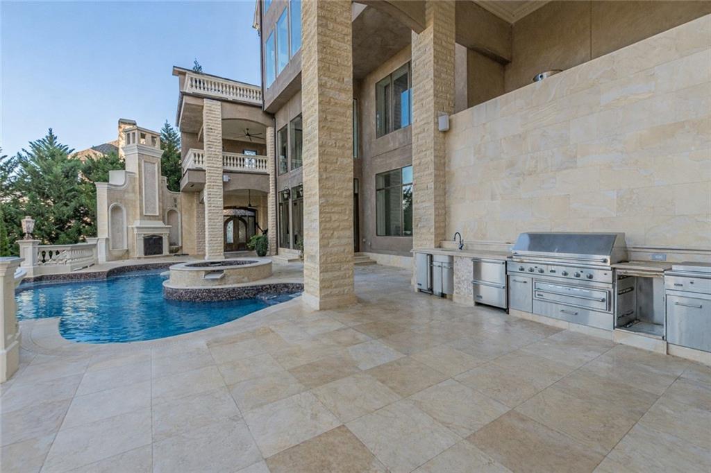 Pool patio with a raised circular spa and built-in stainless-steel outdoor kitchen beside a stone house.