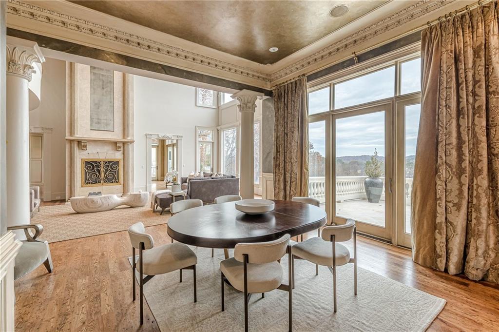 Dining area with a dark oval table, ornate fireplace, and tall windows opening to a terrace.