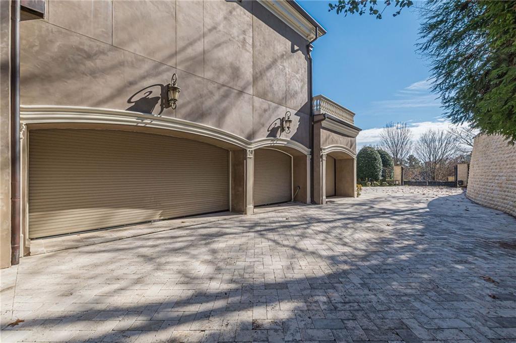 Home exterior with multiple garage doors and a broad paved driveway leading to a gated courtyard.