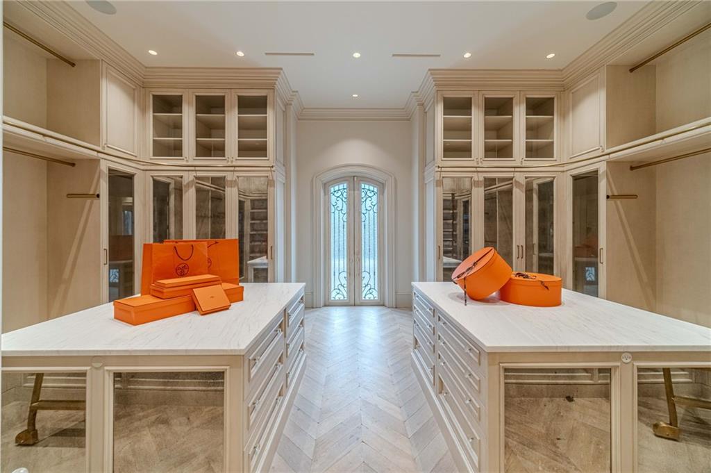 Walk-in closet with marble-topped islands, glass-front cabinetry, and orange boxes and bags.