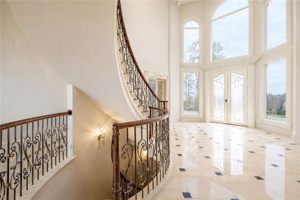 Foyer with a curved iron-railed staircase, marble floor, and tall arched windows.