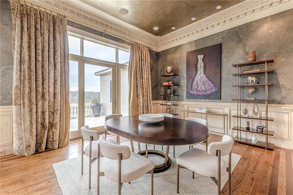 Formal dining room with a round table, tall terrace doors, patterned curtains, and ornate crown molding.
