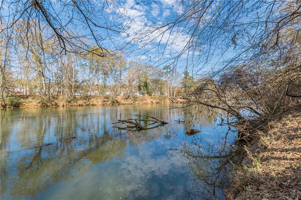 Pond bordered by leafless trees, with clouds reflected on the water.