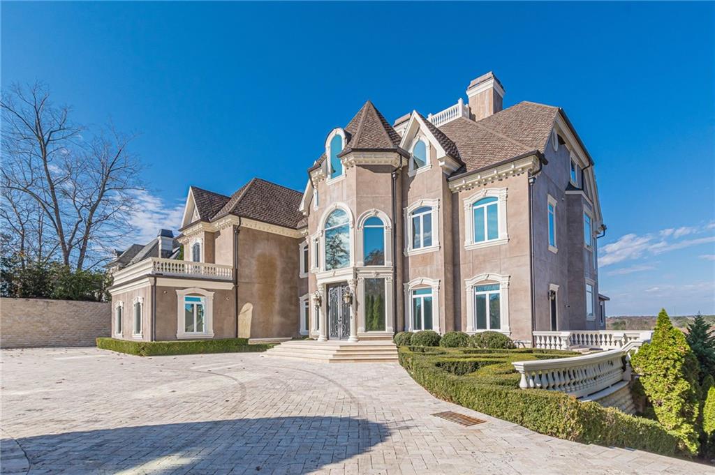 Stucco mansion with turrets, arched windows, and a broad paved driveway.