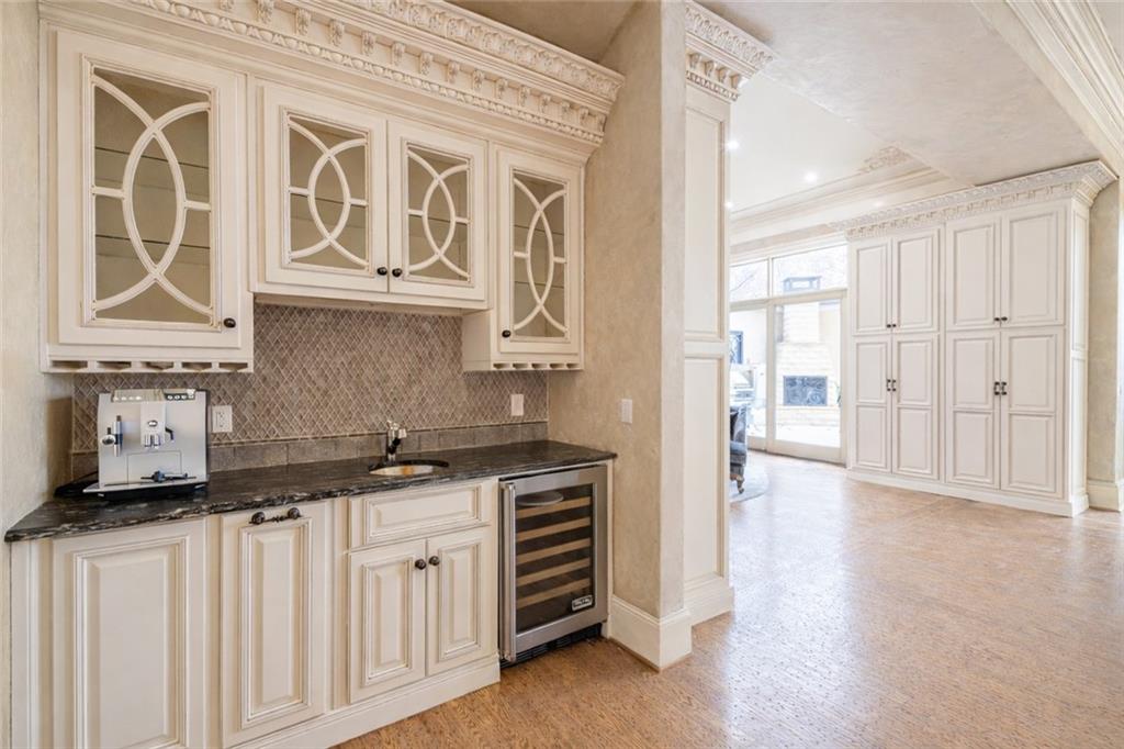 Built-in wet bar with ornate cream cabinetry, dark counters, patterned tile backsplash, and wine refrigerator.