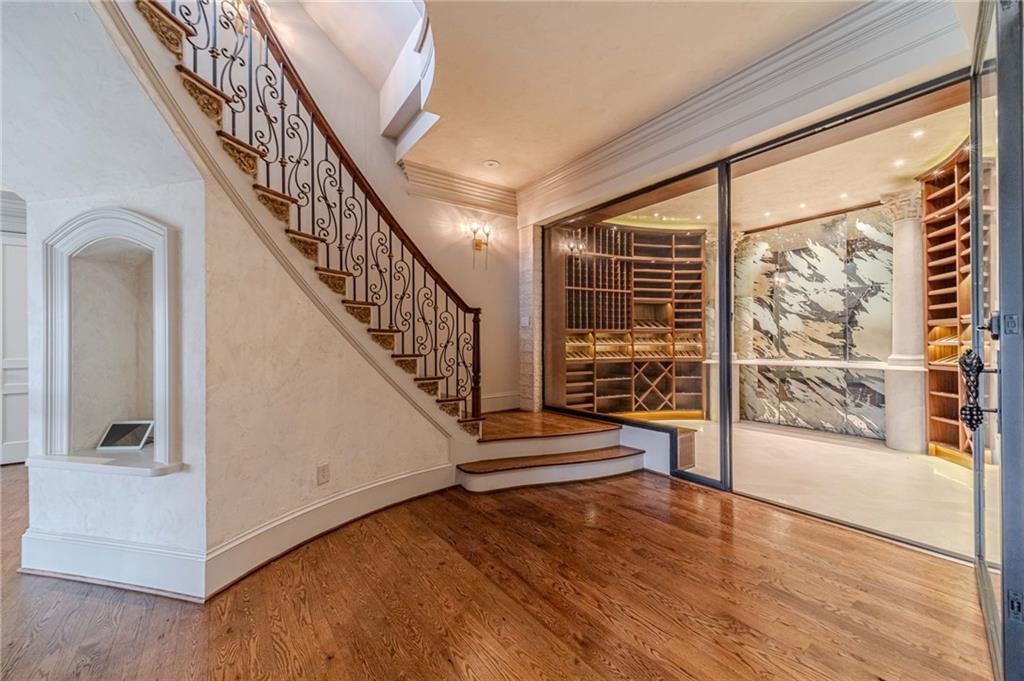 Entryway with an ornate staircase and glass-enclosed wine cellar lined with wooden racks.
