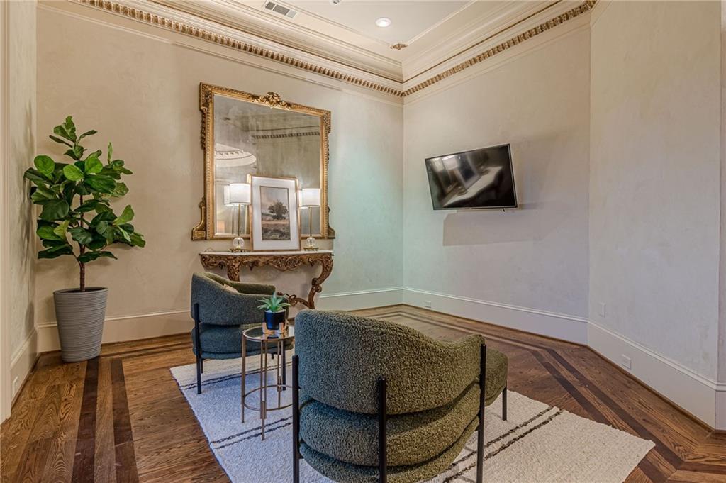 Furnished sitting room with ornate mirror, upholstered chairs, patterned hardwood floors, and wall-mounted television.