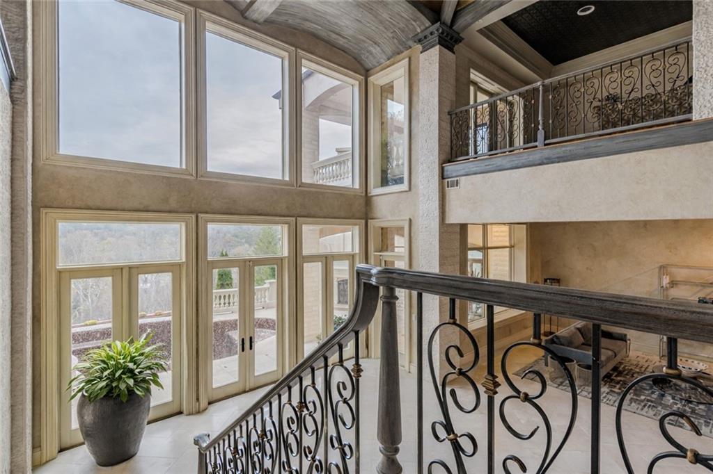 Two-story foyer with tall windows, ornate iron stair railing, and wooded views.