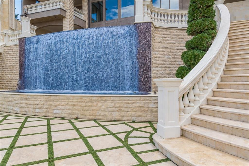 Stone home exterior with a blue water wall fountain and sweeping curved staircase.