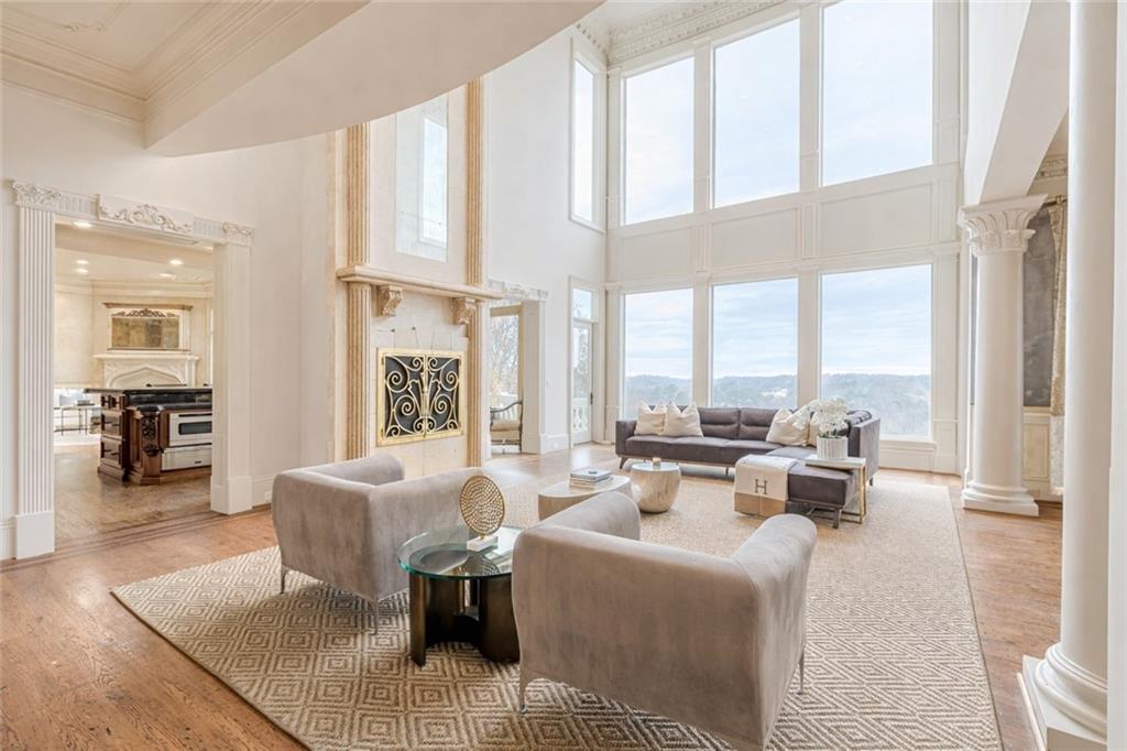 Staged living room with soaring ceilings, tall windows, fireplace, and neutral seating.