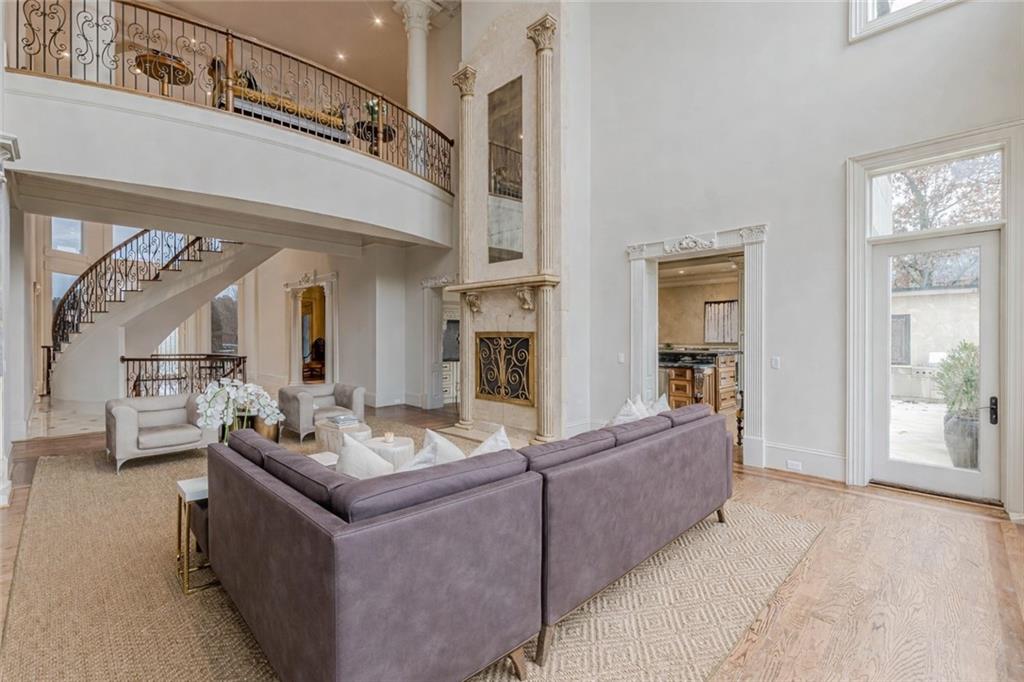 Two-story living room with a curved staircase, ornate fireplace, and gray sectional sofa.