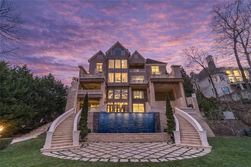 Large stone residence with twin curved staircases and a rectangular water feature at dusk.