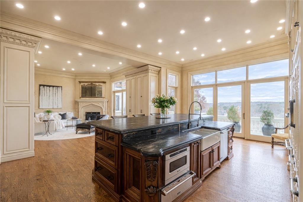 Kitchen with a large dark stone island, rich wood cabinetry, and tall windows overlooking trees.