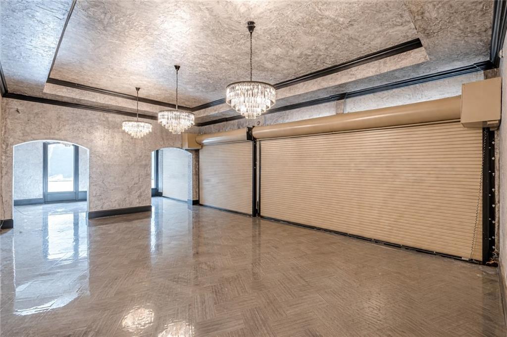 Vacant room with two roll-up doors, polished flooring, and crystal chandeliers.