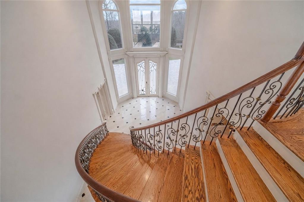 Curved oak staircase overlooks a tiled foyer with a decorative glass door and tall arched windows.