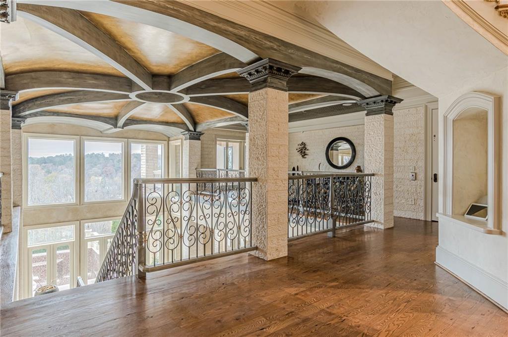 Upper landing with an ornate coffered ceiling, wrought-iron railings and views of trees through tall windows.