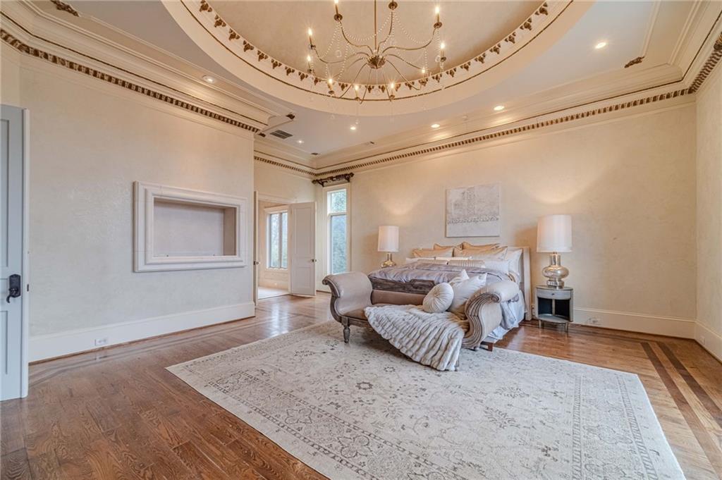Spacious bedroom with an ornate ceiling medallion, chandelier, hardwood floors, and a large patterned rug.
