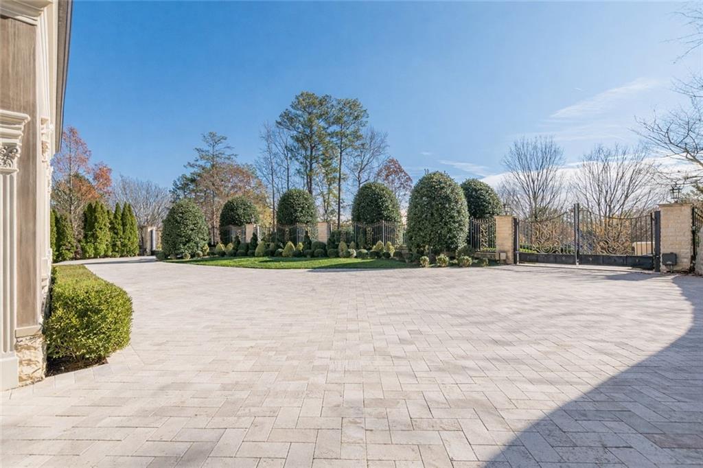 Paved driveway courtyard with clipped shrubs and a decorative metal gate.
