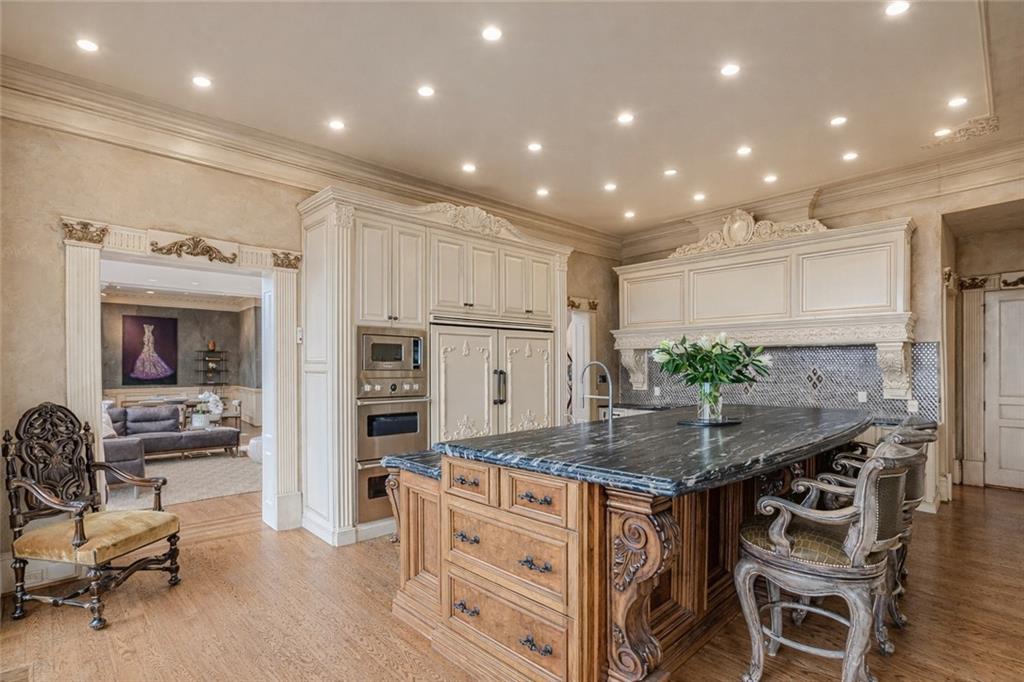 Ornate kitchen with cream cabinetry and a large dark stone island surrounded by carved wood details.