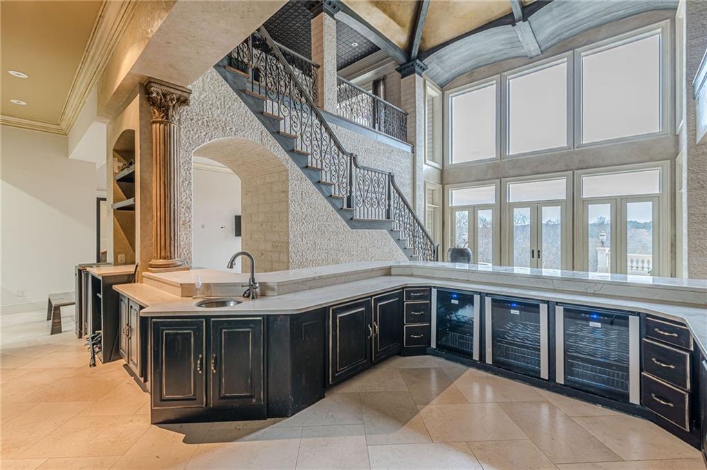 Kitchen with a curved dark-wood island and beverage refrigerators beneath tall windows.