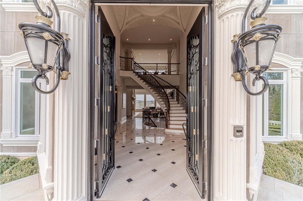 Grand foyer with open wrought-iron doors, a curved staircase, and patterned tile flooring.
