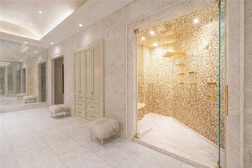 Luxury bathroom with a gold mosaic walk-in shower, marble finishes, built-in cabinetry, and upholstered stools.