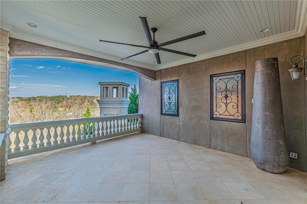 Covered porch with a black ceiling fan and tiled floor overlooking wooded hills.