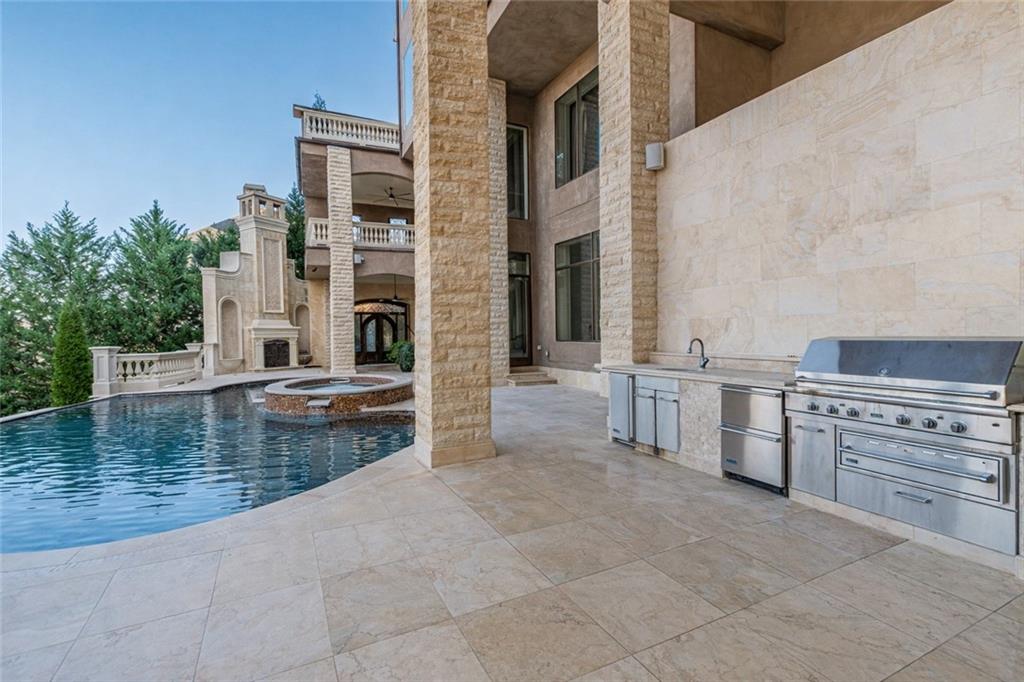 Outdoor pool and raised spa beside a stone patio with a built-in stainless steel grill.