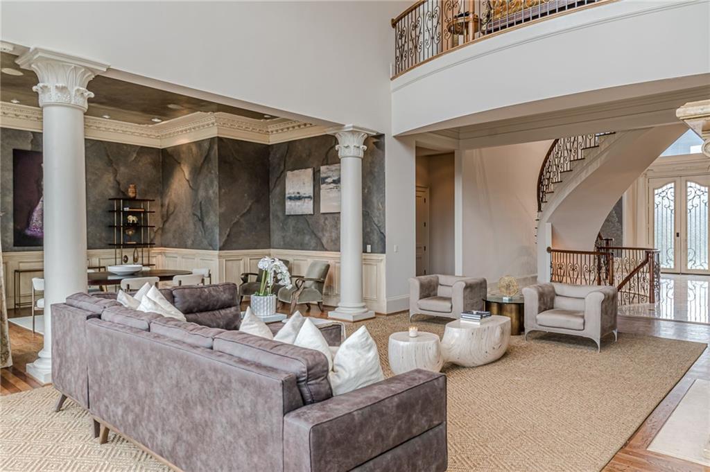 Two-story living room with a gray sectional, marble accent walls, white columns, and a curved staircase.