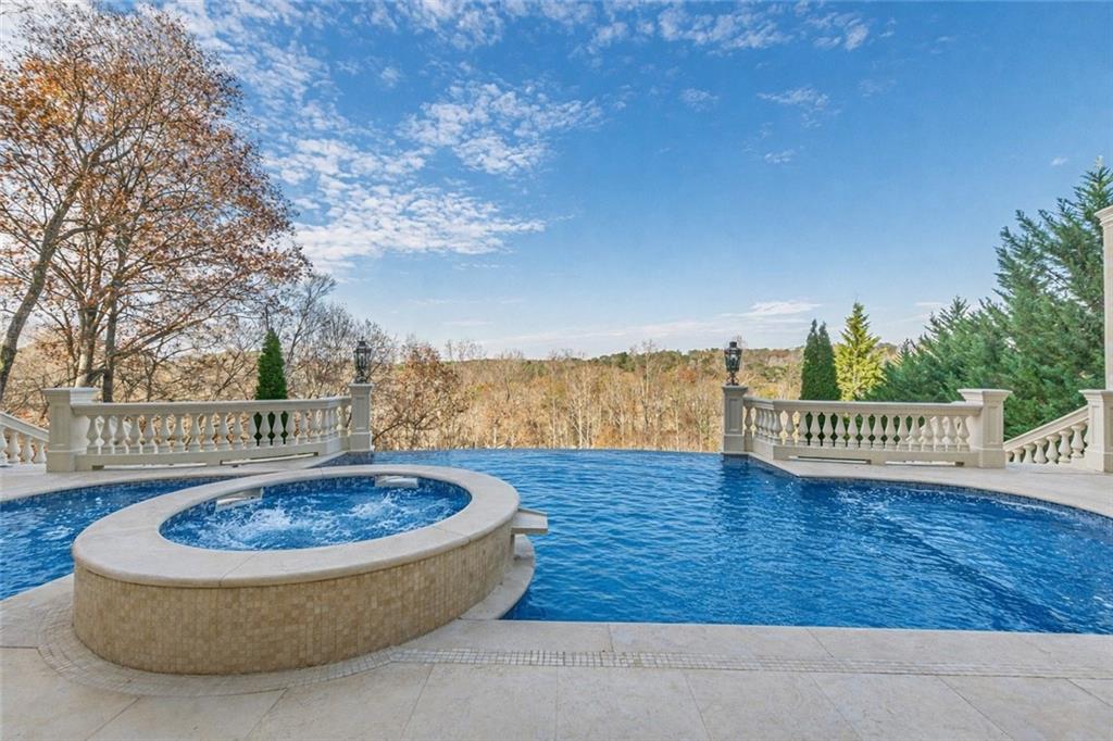 Swimming pool and raised circular spa overlooking wooded trees, bordered by pale stone balustrades.