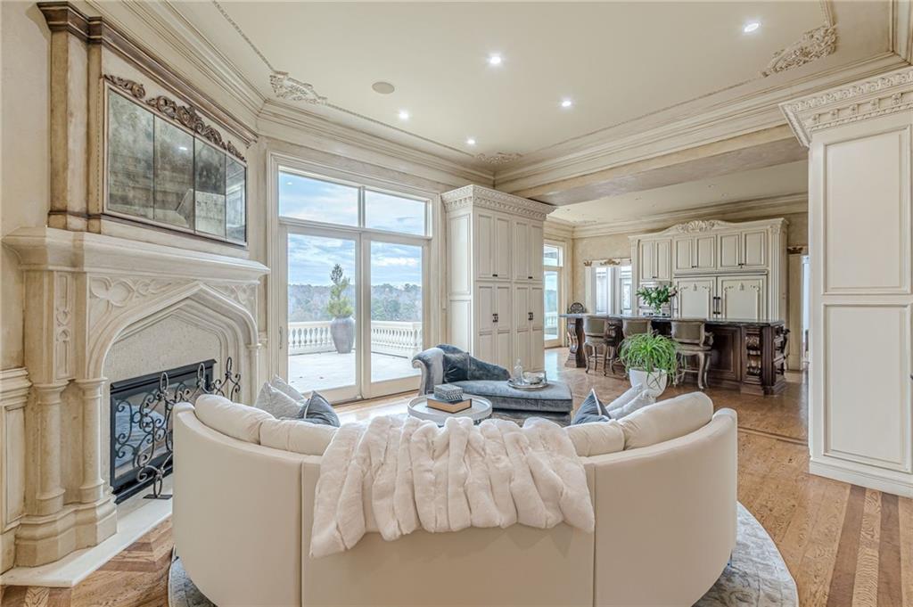 Living room with an ornate stone fireplace, curved white sofa, and large windows overlooking trees.