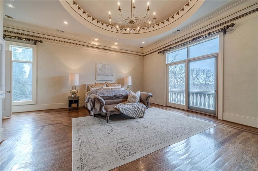 Furnished bedroom with a chandelier, hardwood floors, and glass doors to a tree-lined balcony.