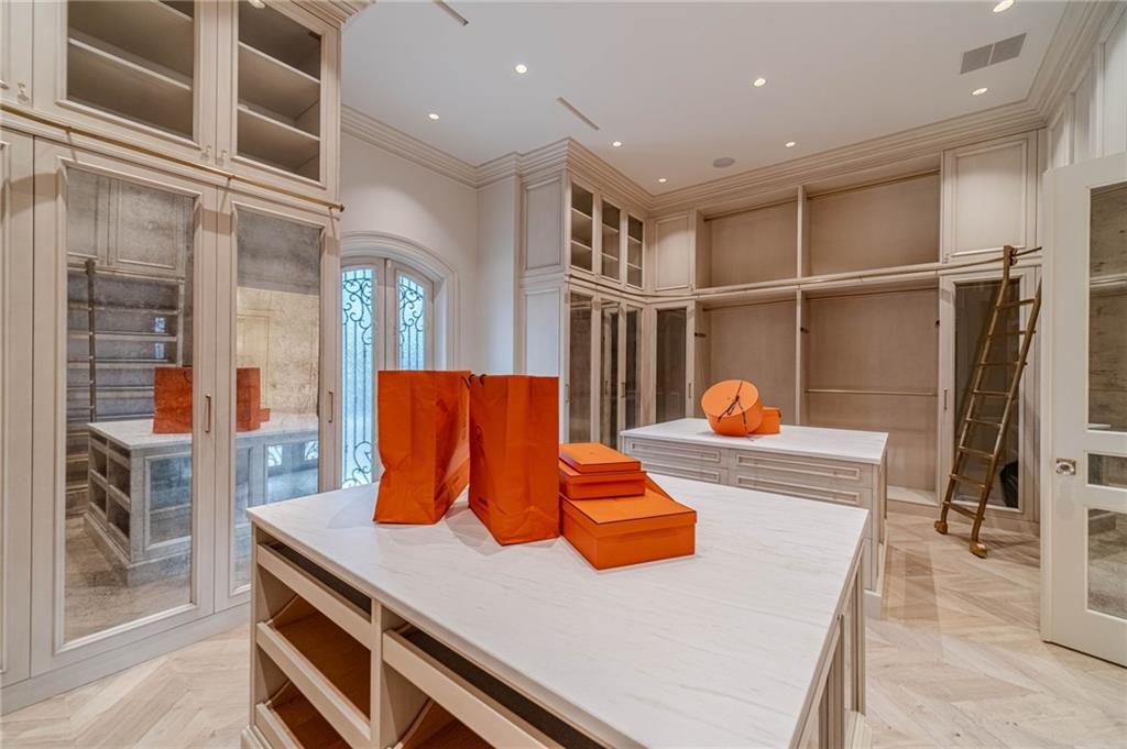 Walk-in closet with glass-fronted cabinetry, marble-topped islands, and orange shopping bags.